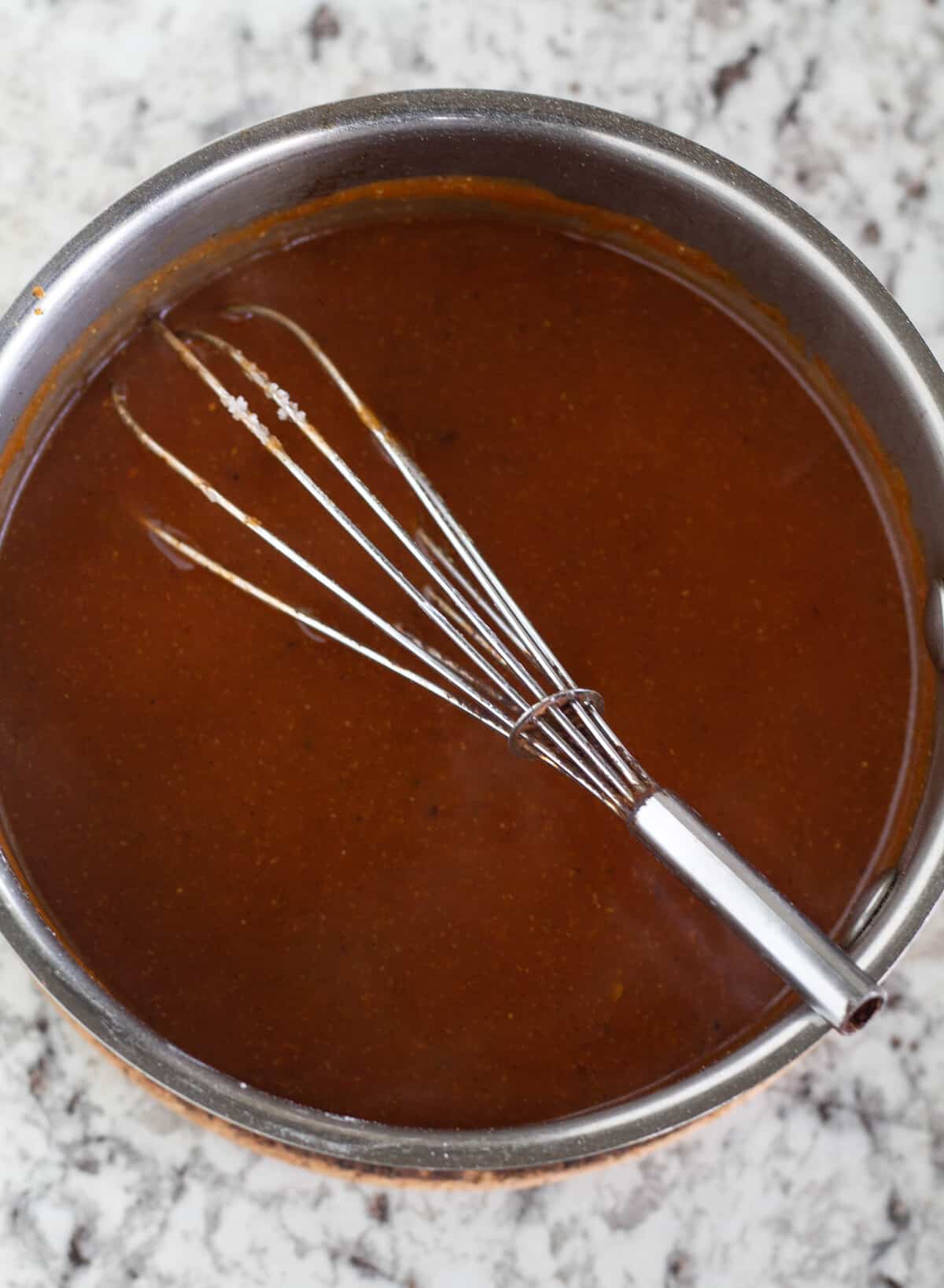 Overhead shot of enchilada sauce in saucepan with whisk.