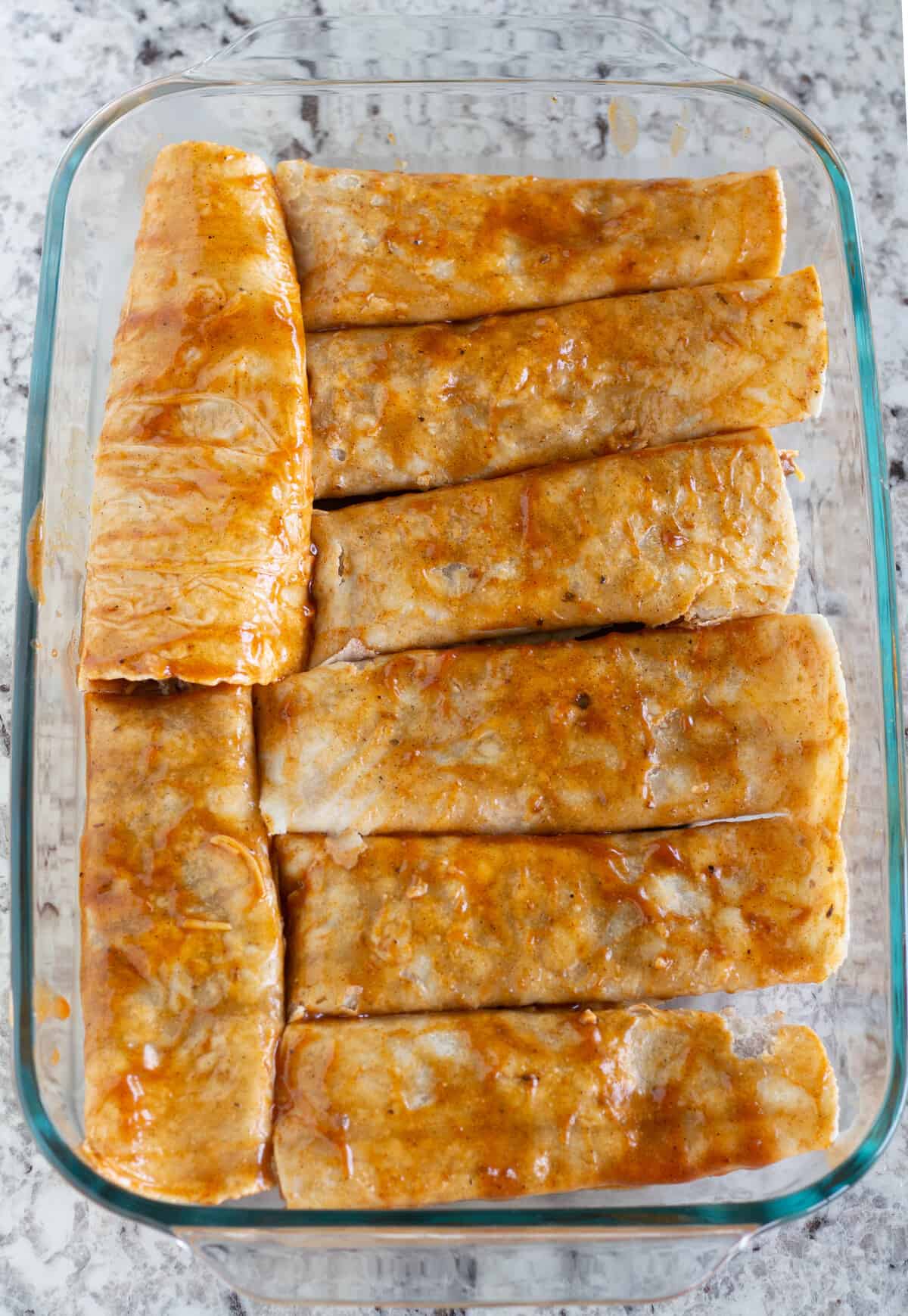 rolled and unbaked enchiladas in baking dish.