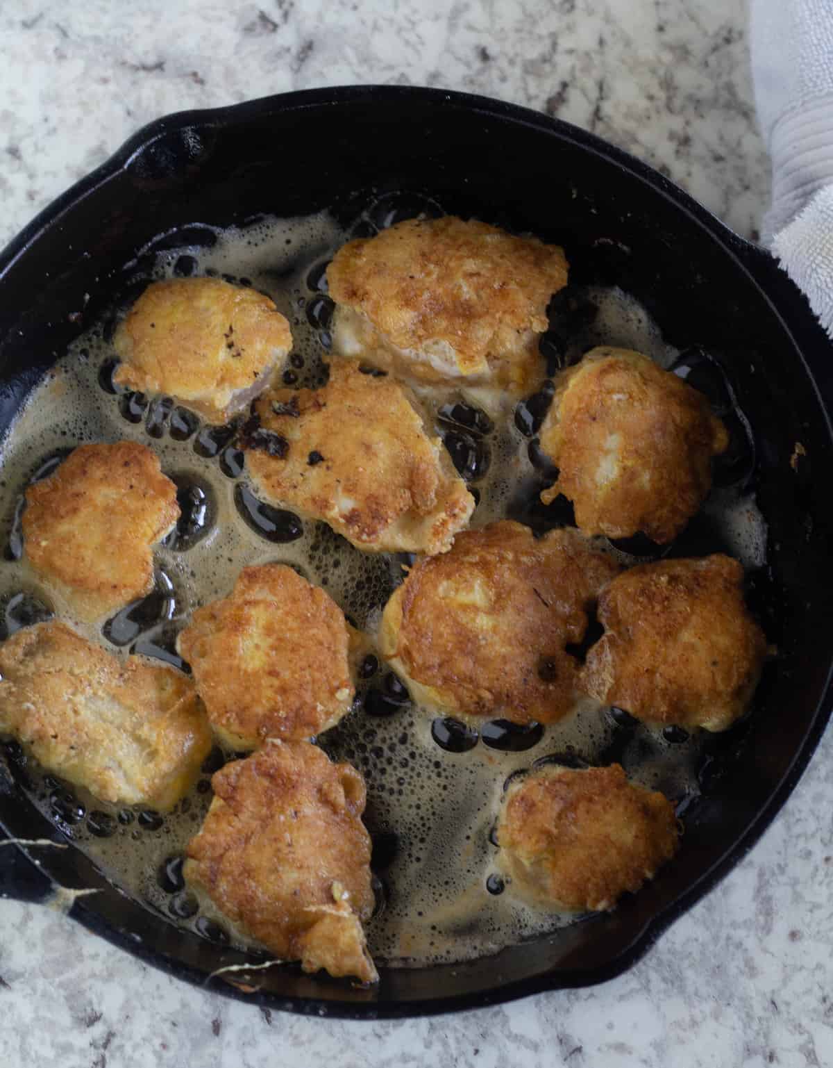 breaded chicken being browned in cast iron skillet