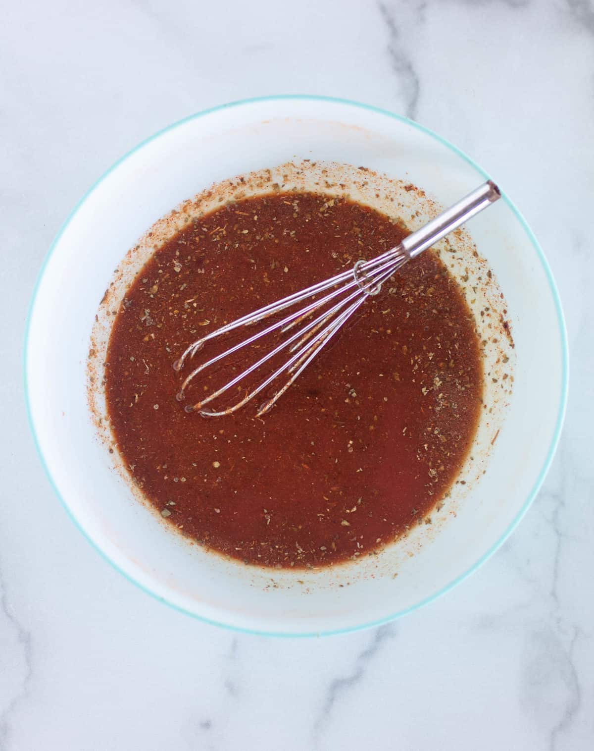 tomato sauce, water, and spices in mixing bowl with whisk