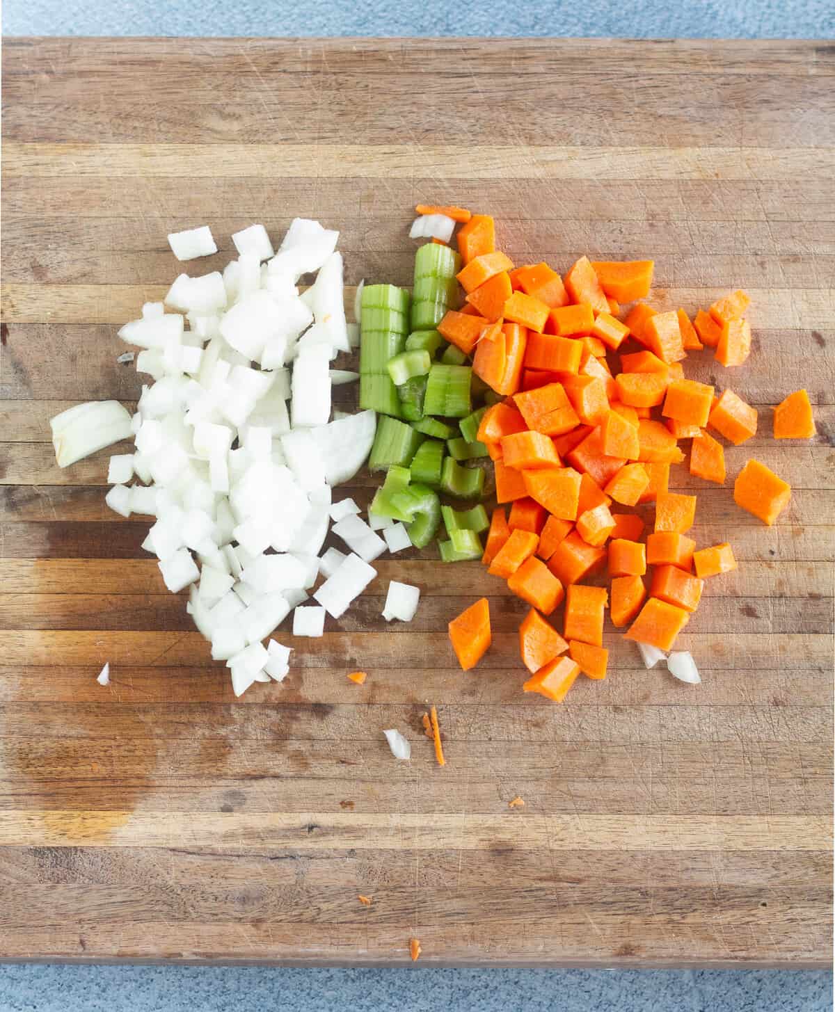 Overhead shot of chopped carrots, celery, and onion on a cutting board.