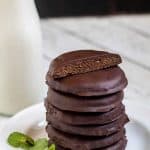 Thin mints stacked on a white plate with milk in the background