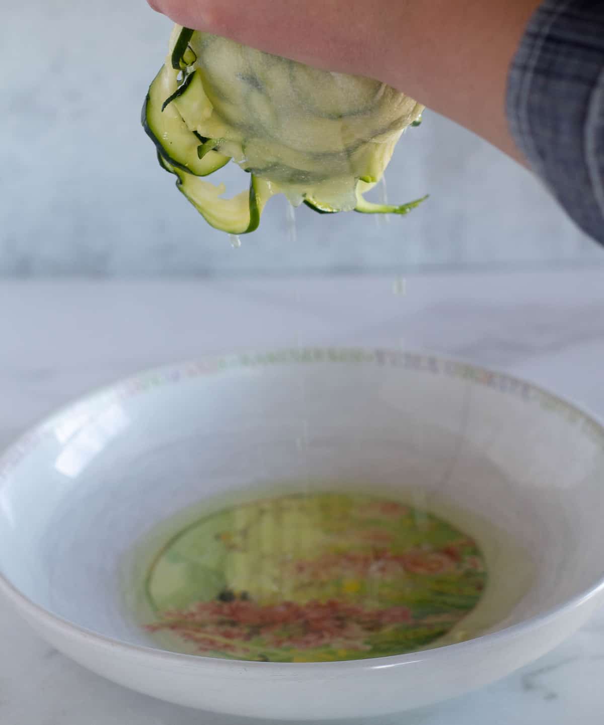 squeezing water out of zucchini noodles into a bowl