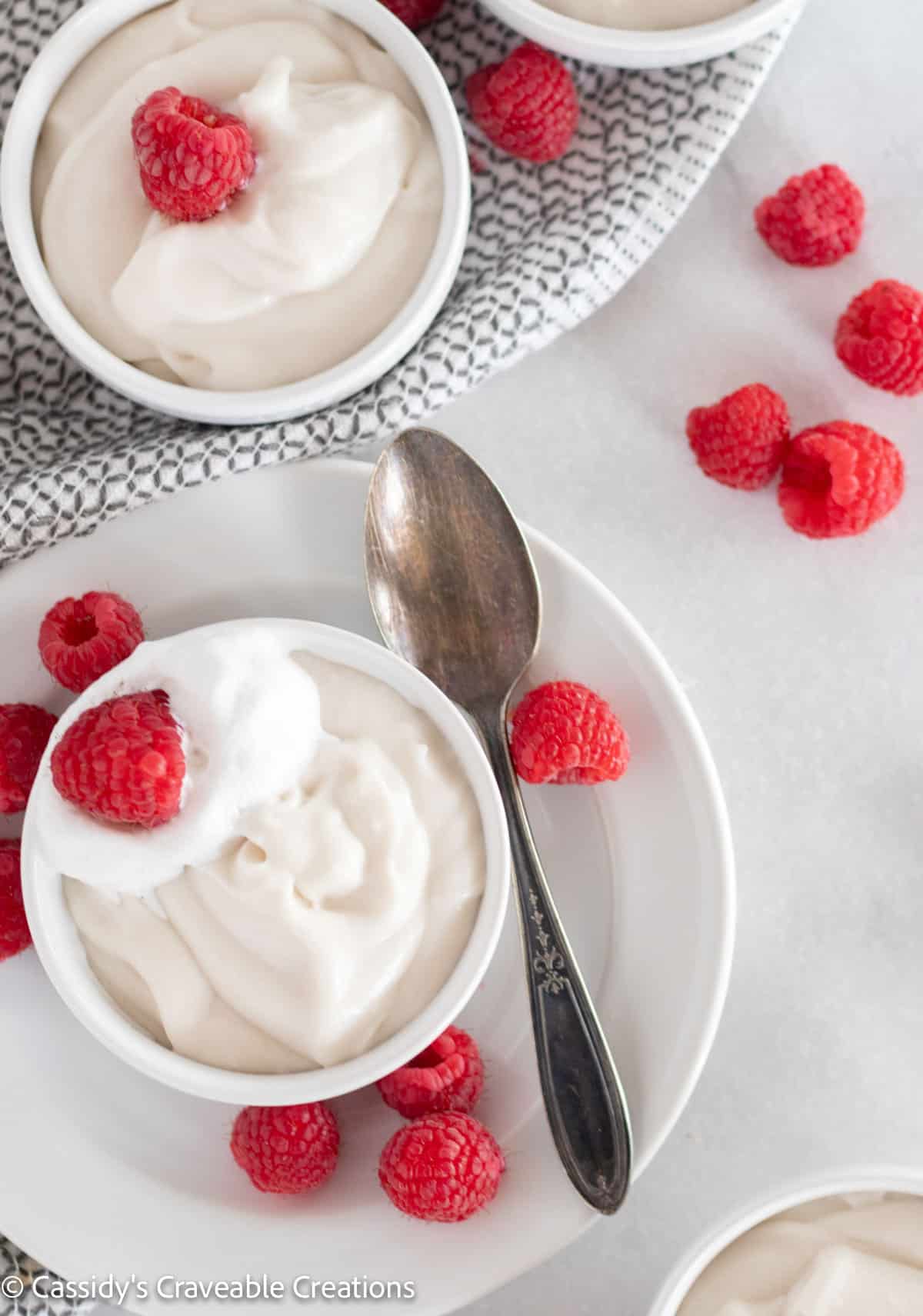 overhead shot of vanilla pudding in bowls with raspberries and a spoon.