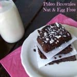 paleo, nut, and egg free brownies stacked on white plate with parchment between each brownie