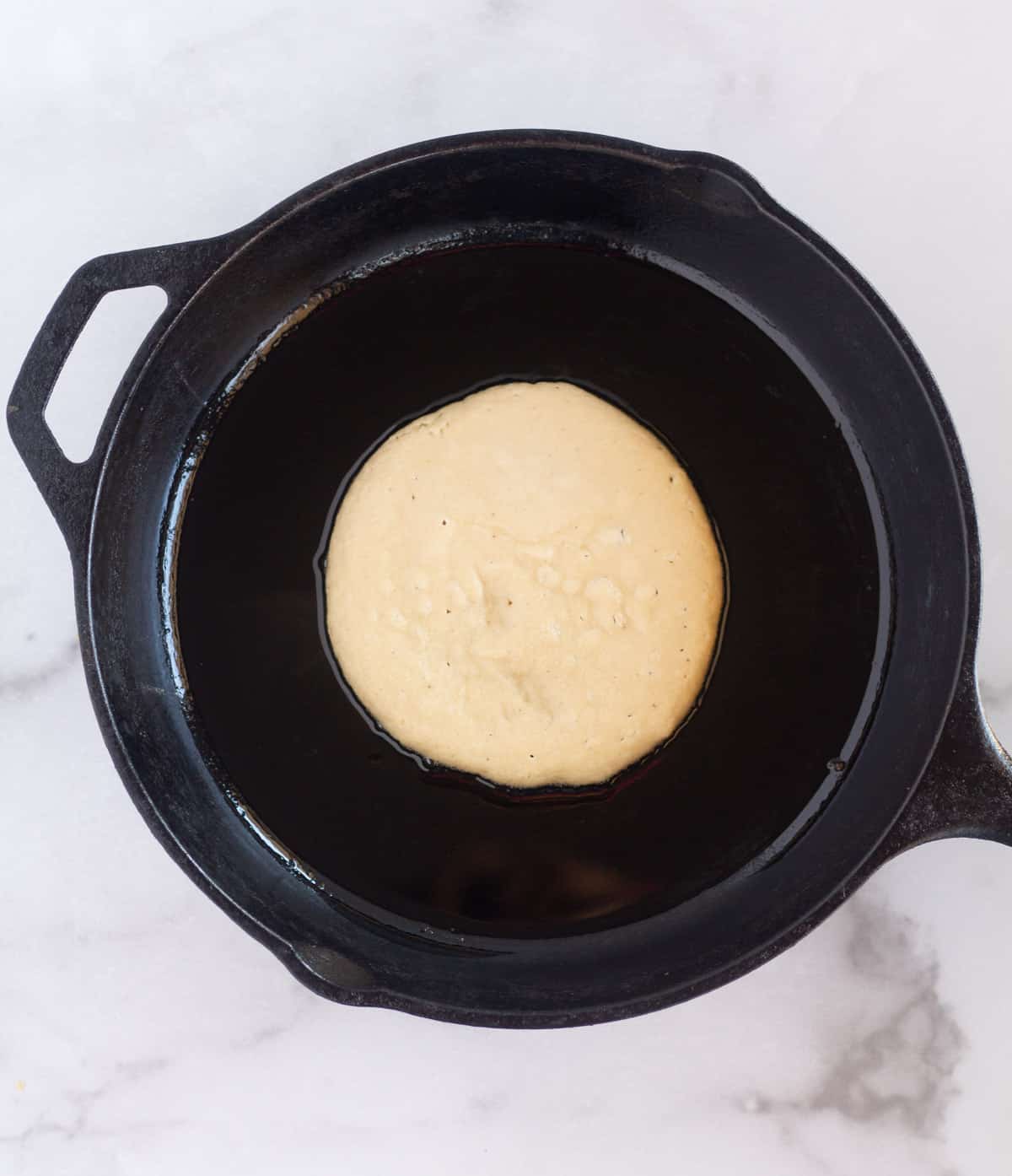 pancake cooking in cast iron skillet before flipping