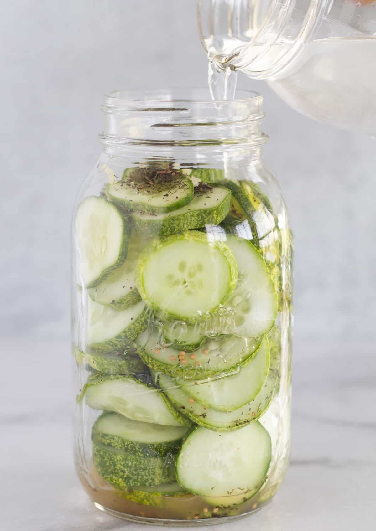 pouring saltwater into a mason jar of sliced cucumbers with spices