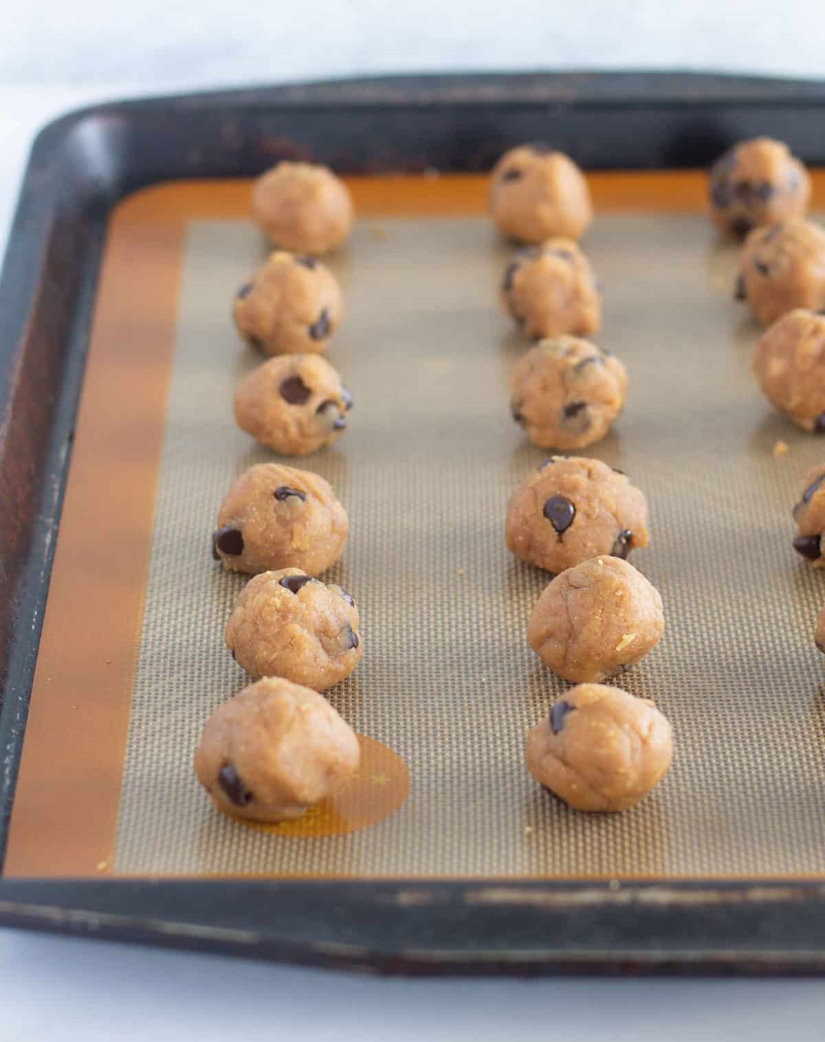 Dough rolled into balls on lined baking sheet.