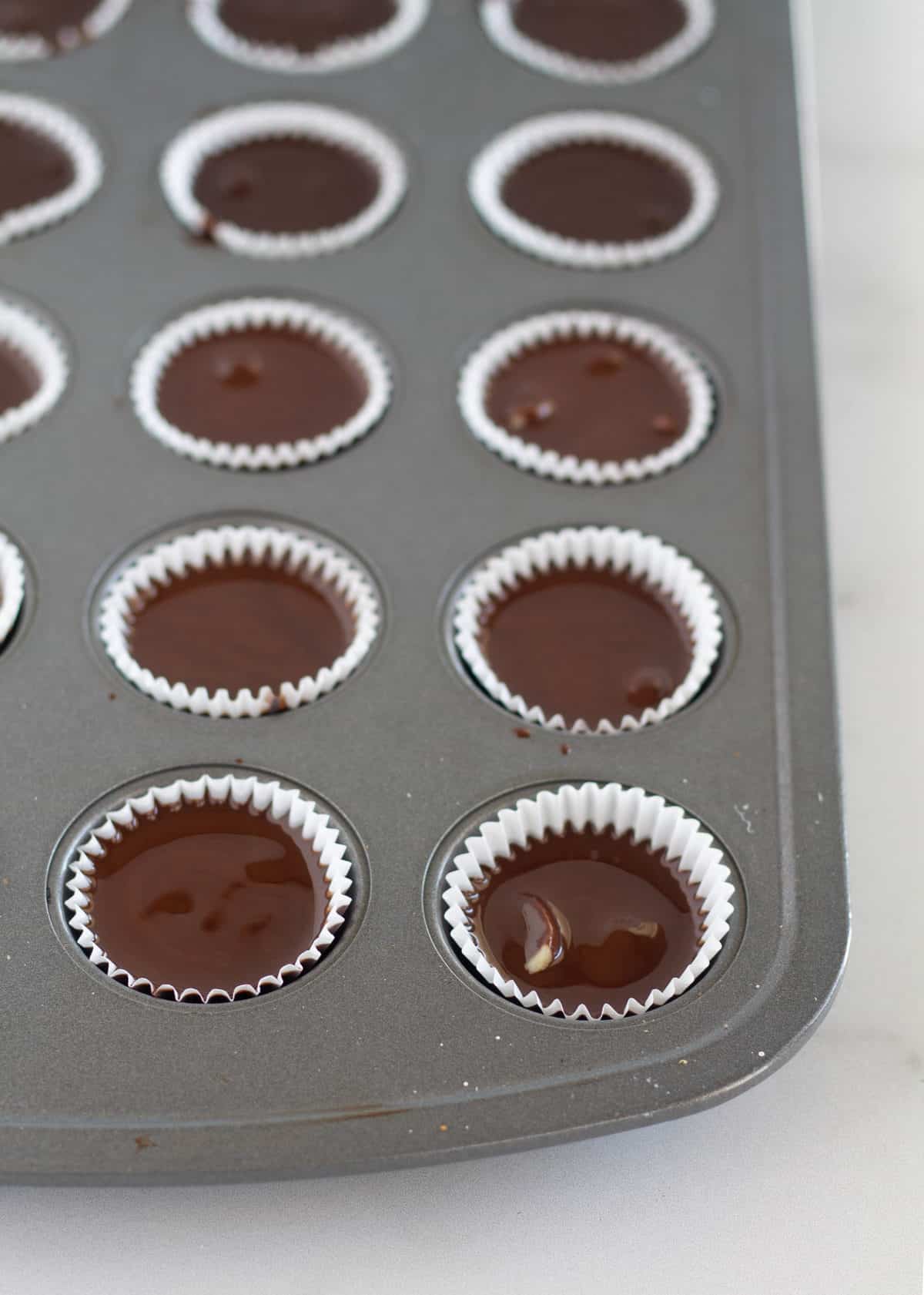 Melted chocolate drizzled over macadamia nuts in mini muffin tin.