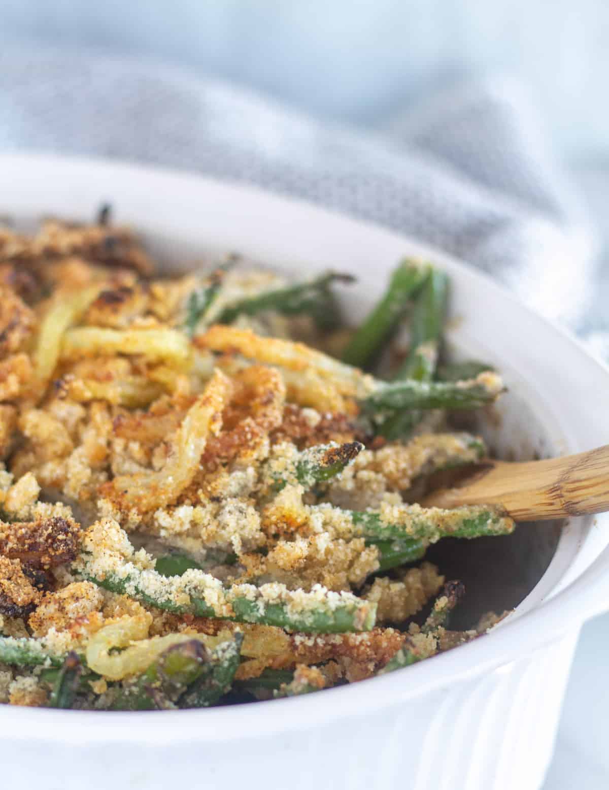side shot of green bean casserole in baking dish with a wooden spoon