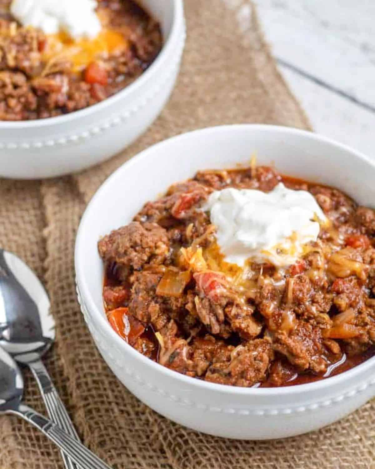 chili in a white bowl with sour cream and shredded cheese.