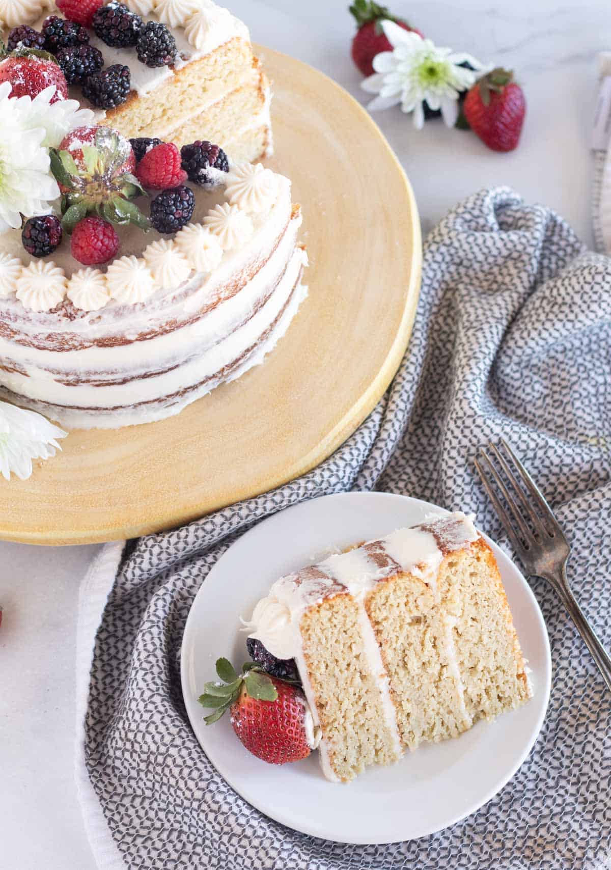 slice of cake with berries on a plate next to cake on stand
