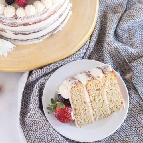 slice of cake on white plate with berries and cake in the background