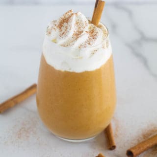 keto, paleo, & vegan pumpkin smoothie in clear glass with whipped cream and cinnamon sticks