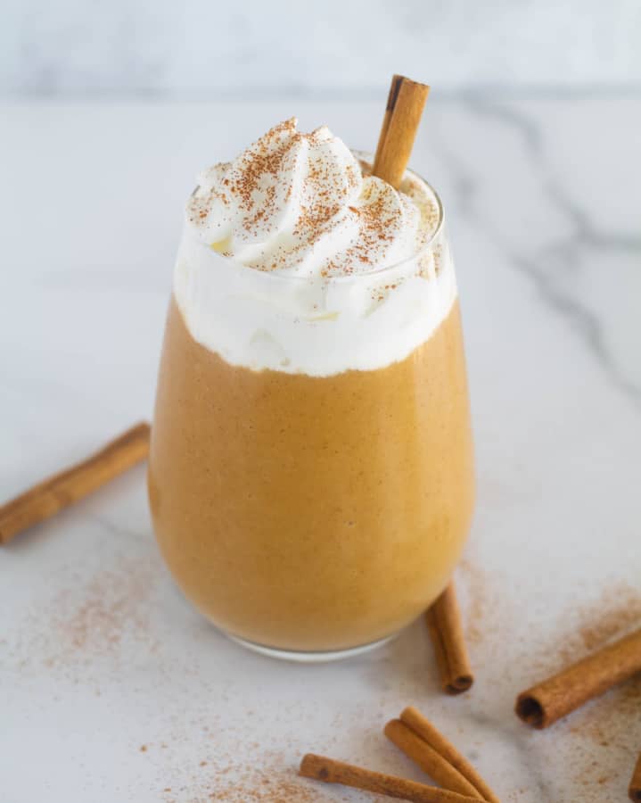 Smoothie on countertop with whipped cream and cinnamon sticks.