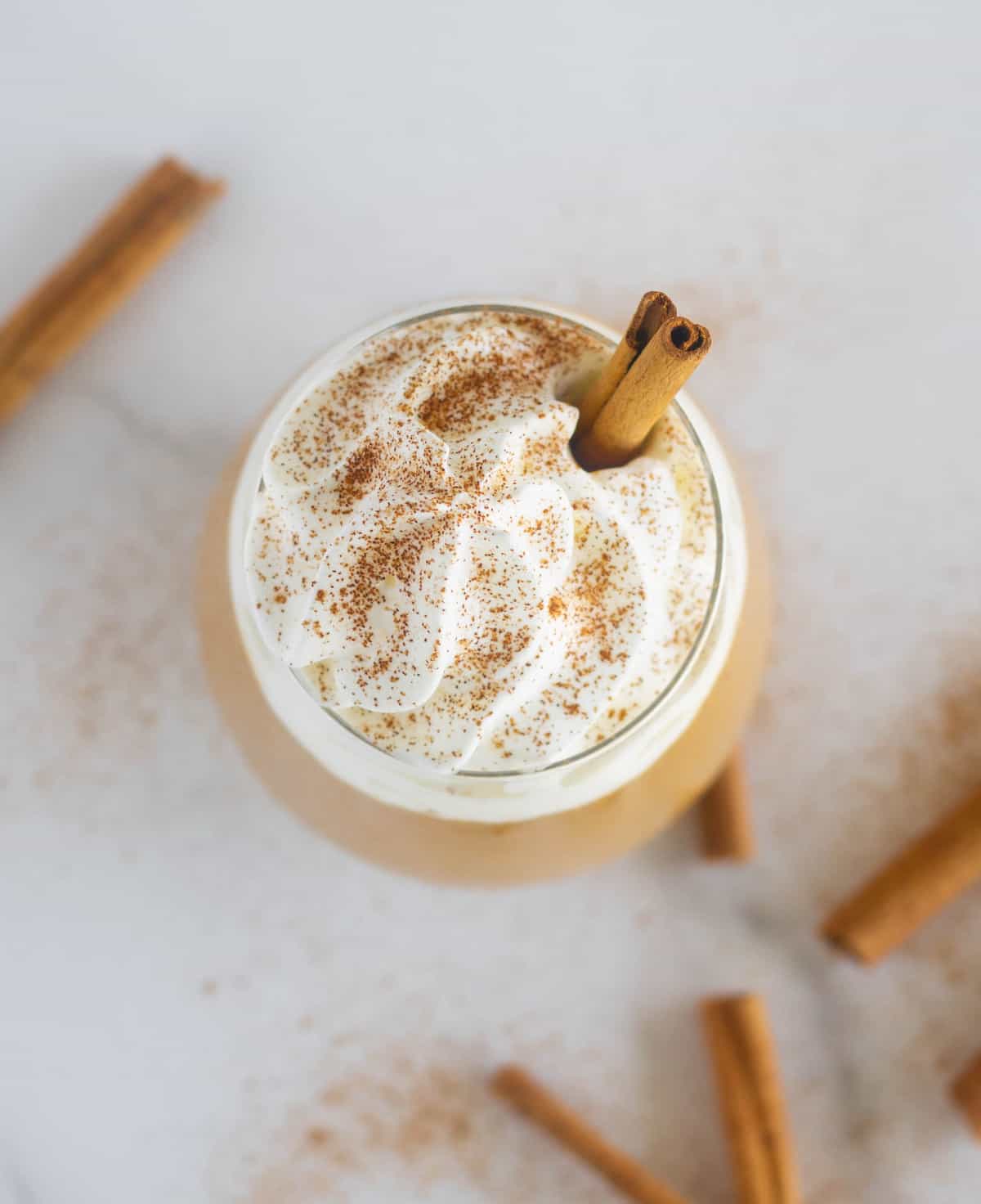 Overhead shot of smoothie with whipped cream and cinnamon sticks.