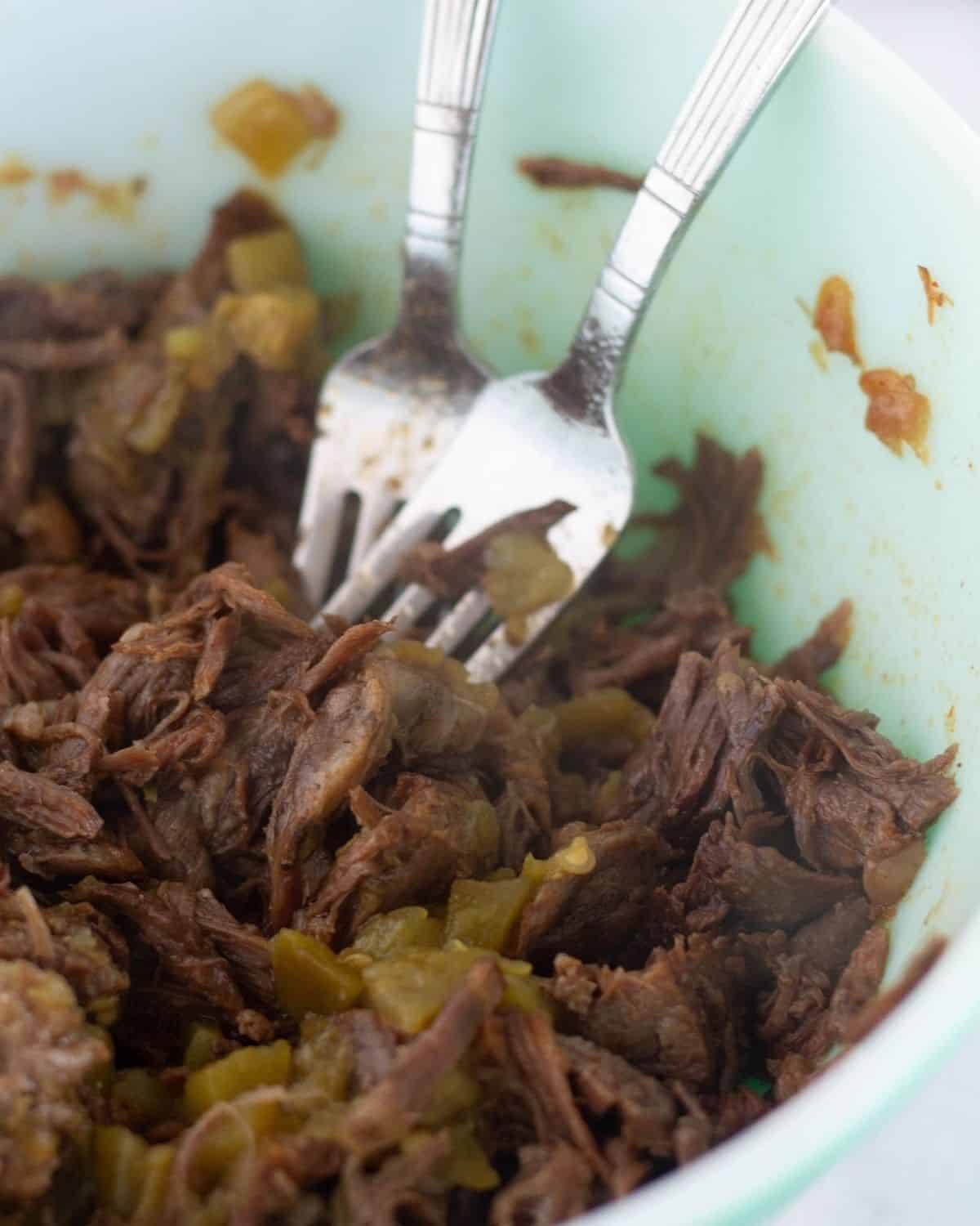 beef in large bowl being shredded with 2 forks