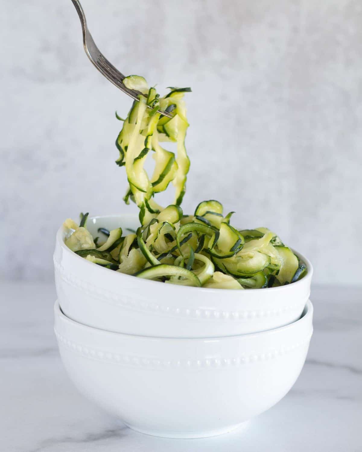 scooping zoodles with fork out of white bowl