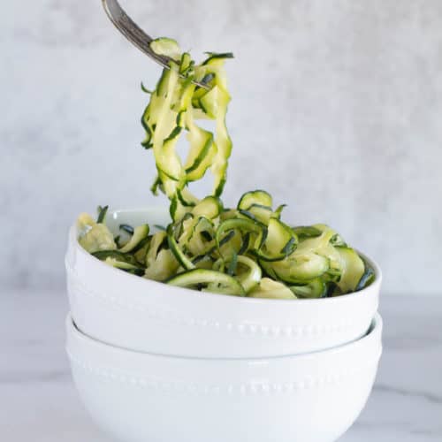 pickup up zucchini noodles out a bowl with a fork