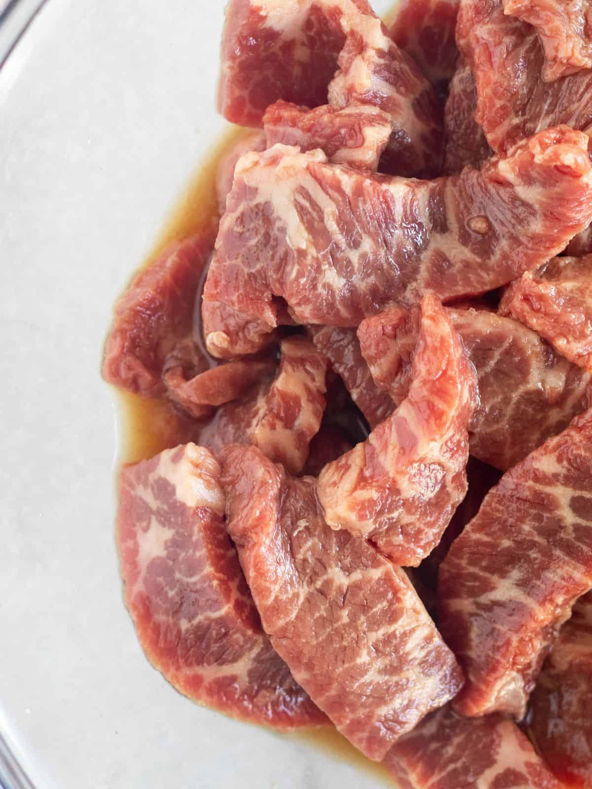 Sliced steak marinating in a clear bowl.,