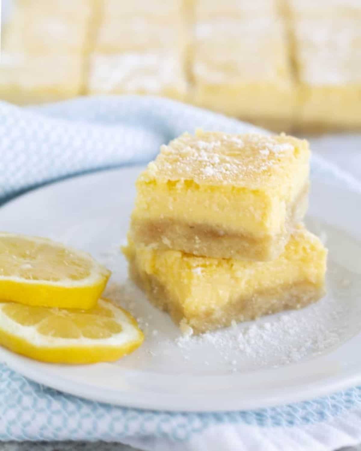 2 lemon squares stacked on plate with lemon slices