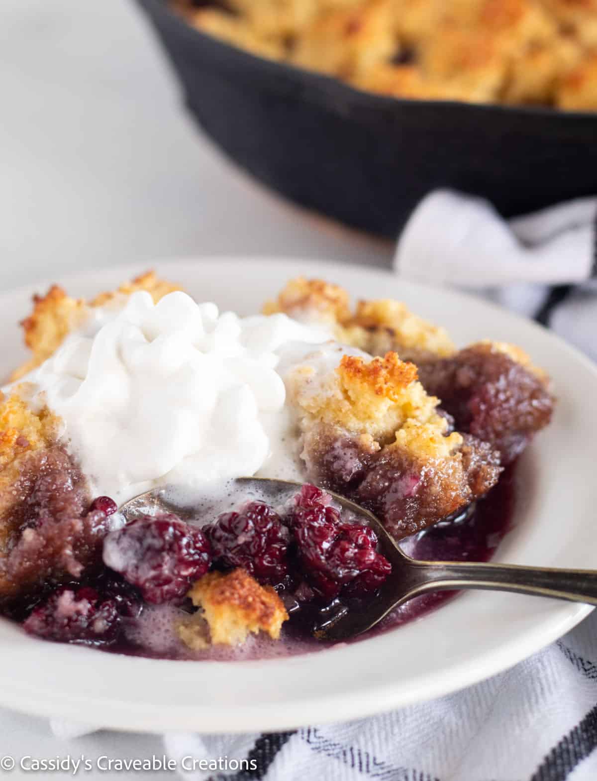 scooping a bite of cobbler from a plate with whipped cream