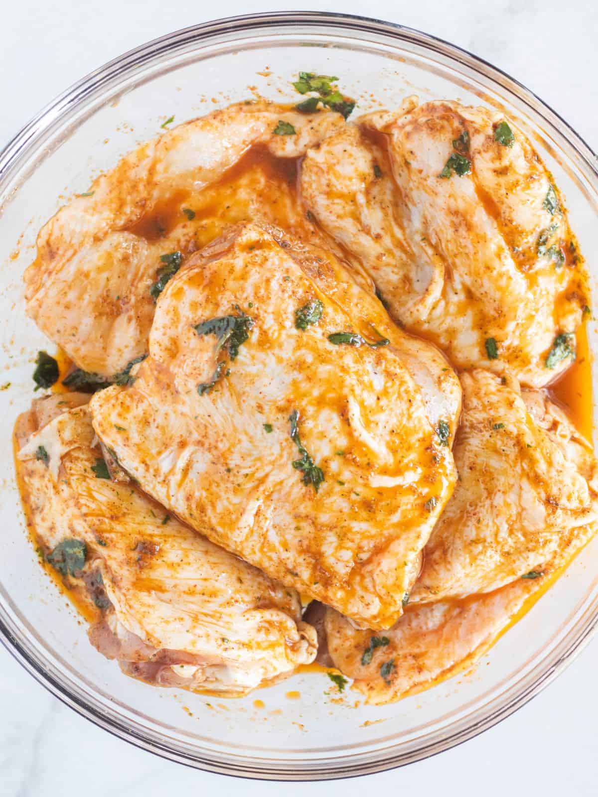 Chicken marinating in a clear bowl.
