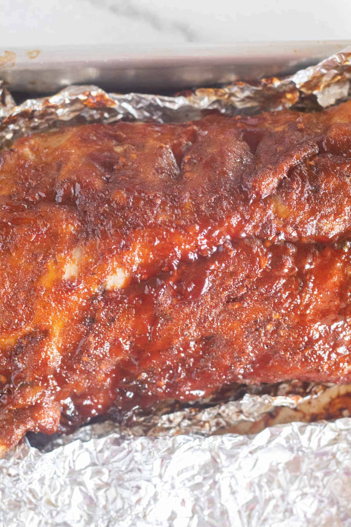 finished ribs with bbq sauce on foil-lined baking sheet