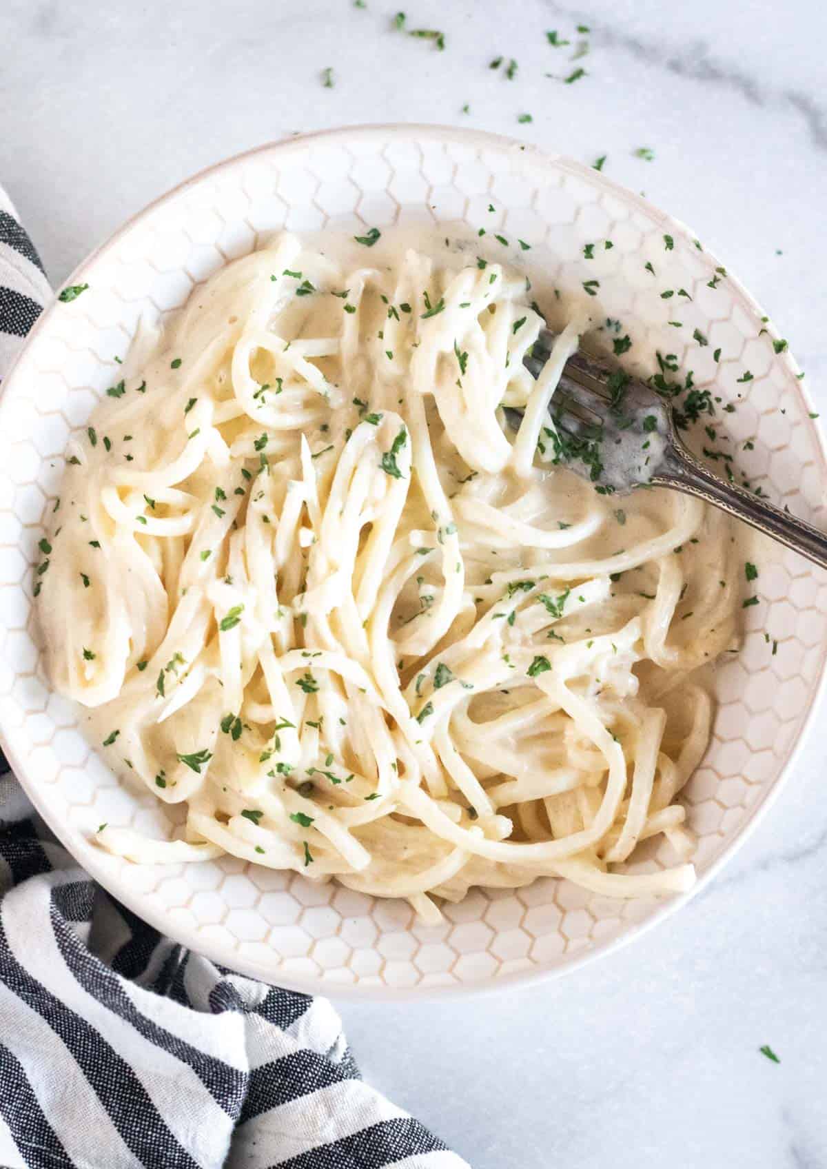 alfredo and palmini noodles tossed together in a bowl with a fork.