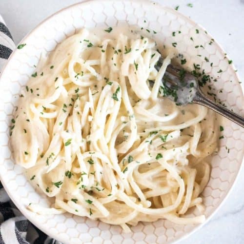 alfredo and noodles tossed together in a bowl with a fork
