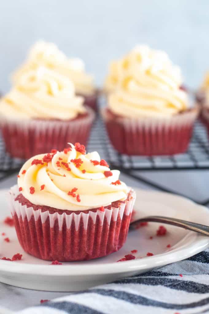red velvet cupcake on white plate with cupcakes in the background