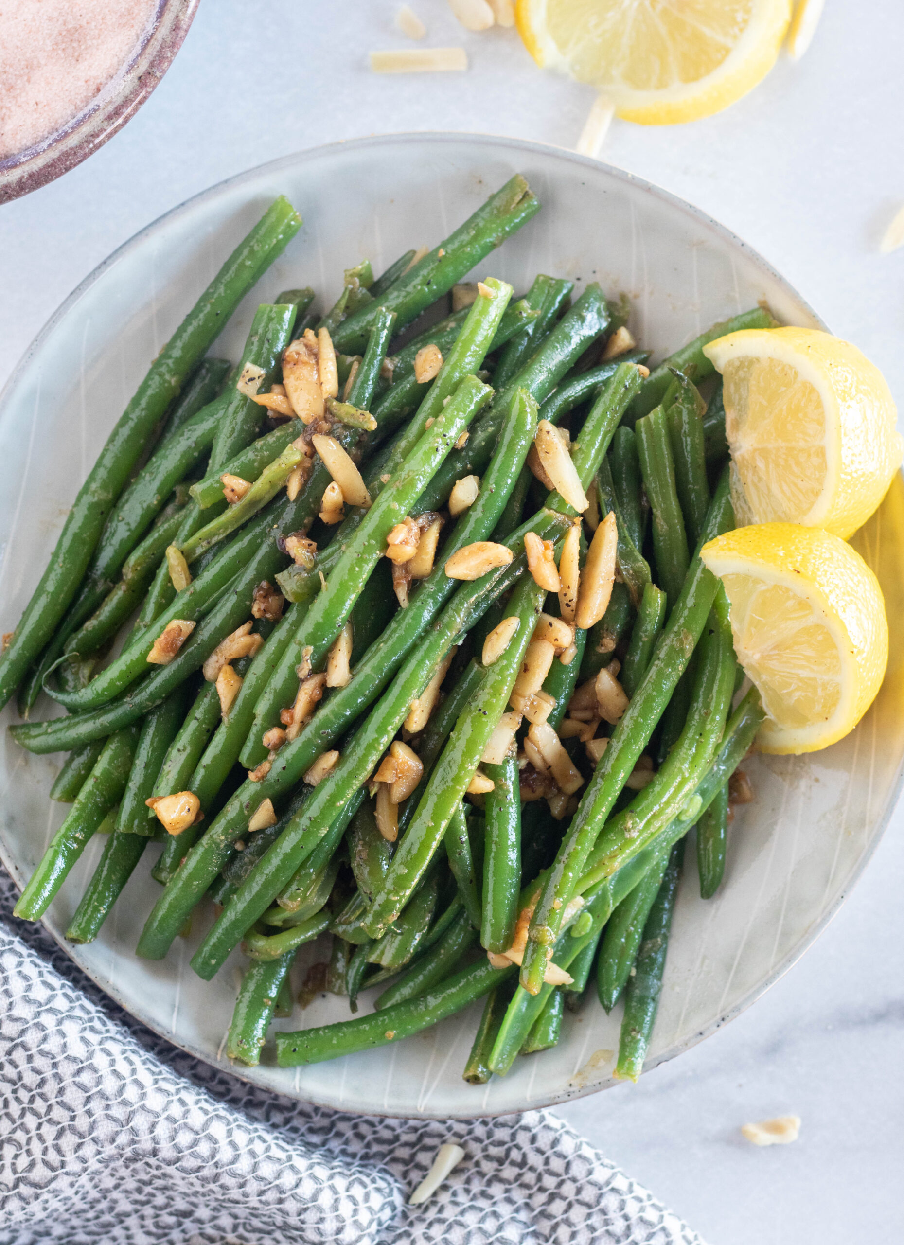 overhead shot of green beans with almonds and lemons on a plate.
