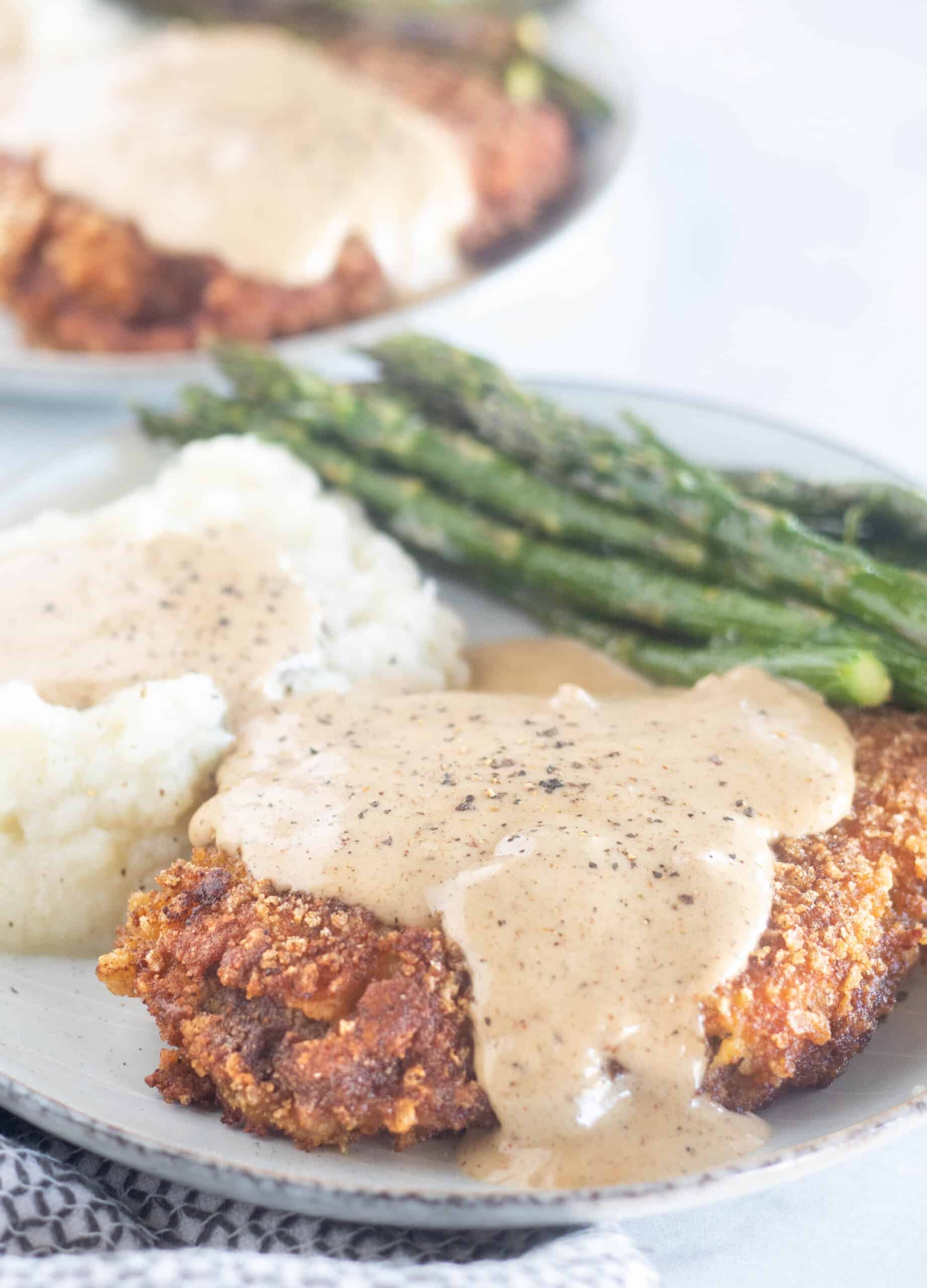 plated chicken fried steak with gravy, mashed cauliflower, and asparagus.