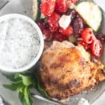 plated greek chicken with sauce and salad
