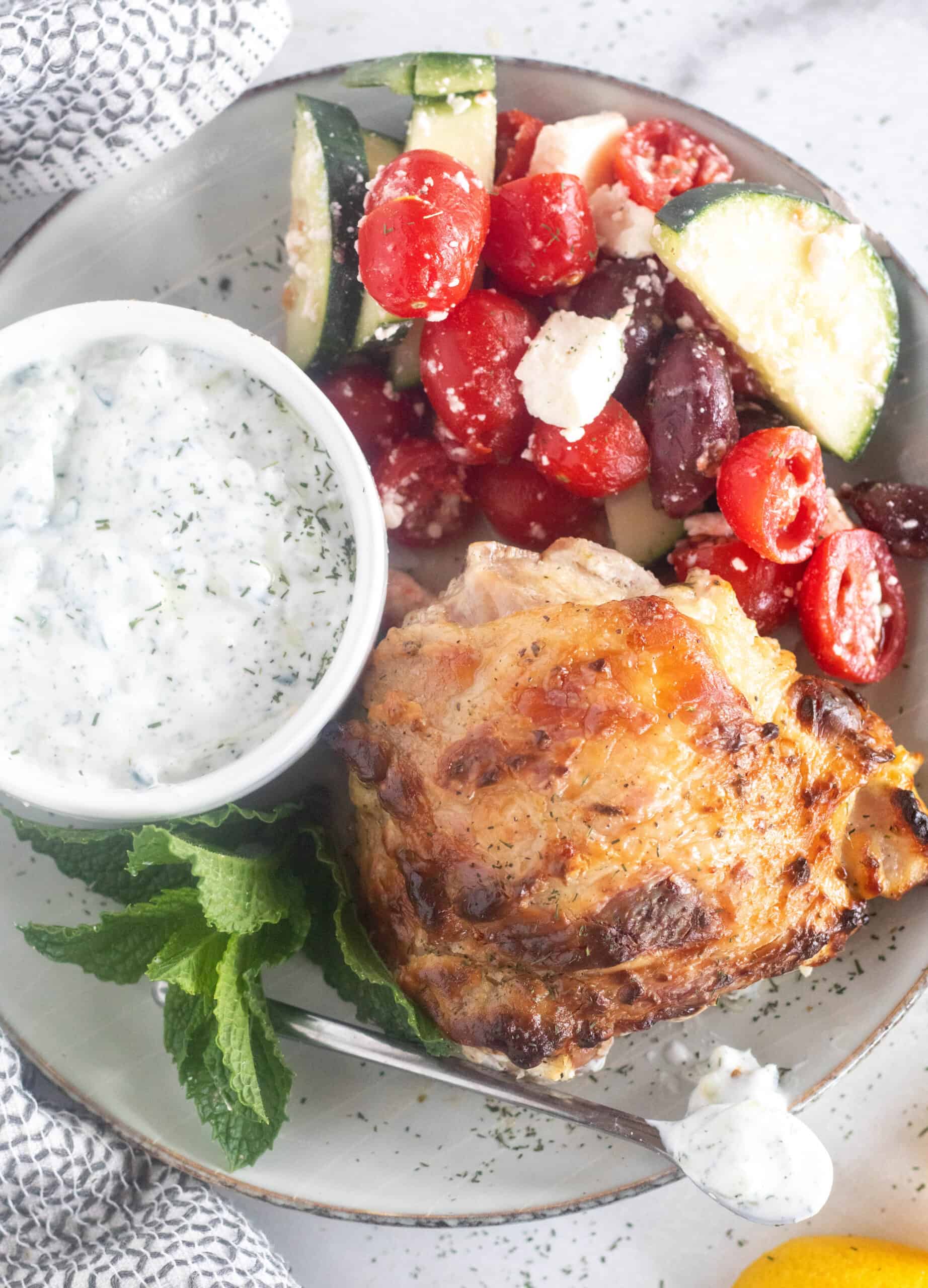 plated greek chicken with sauce and salad