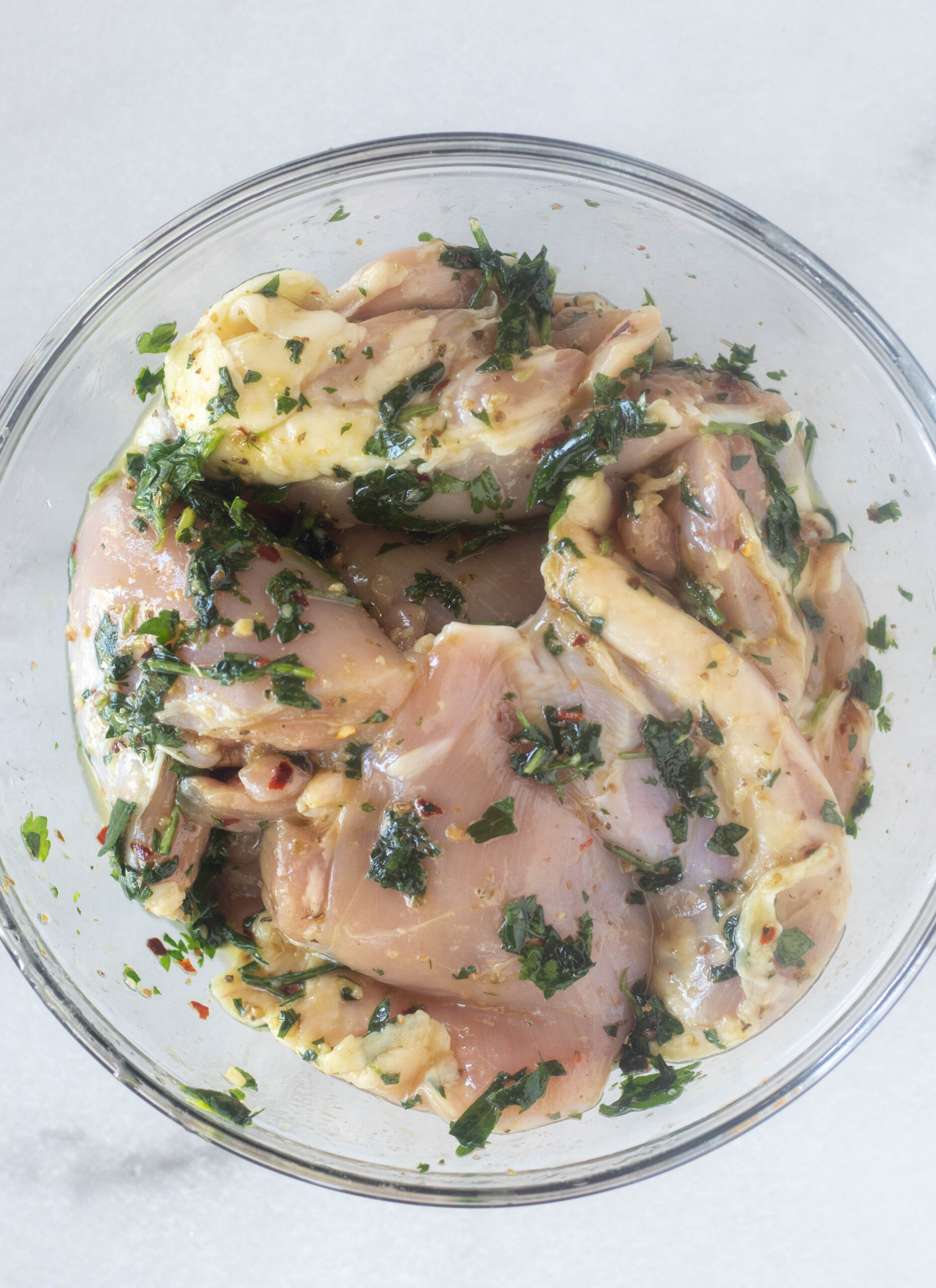 chicken marinating in a clear bowl