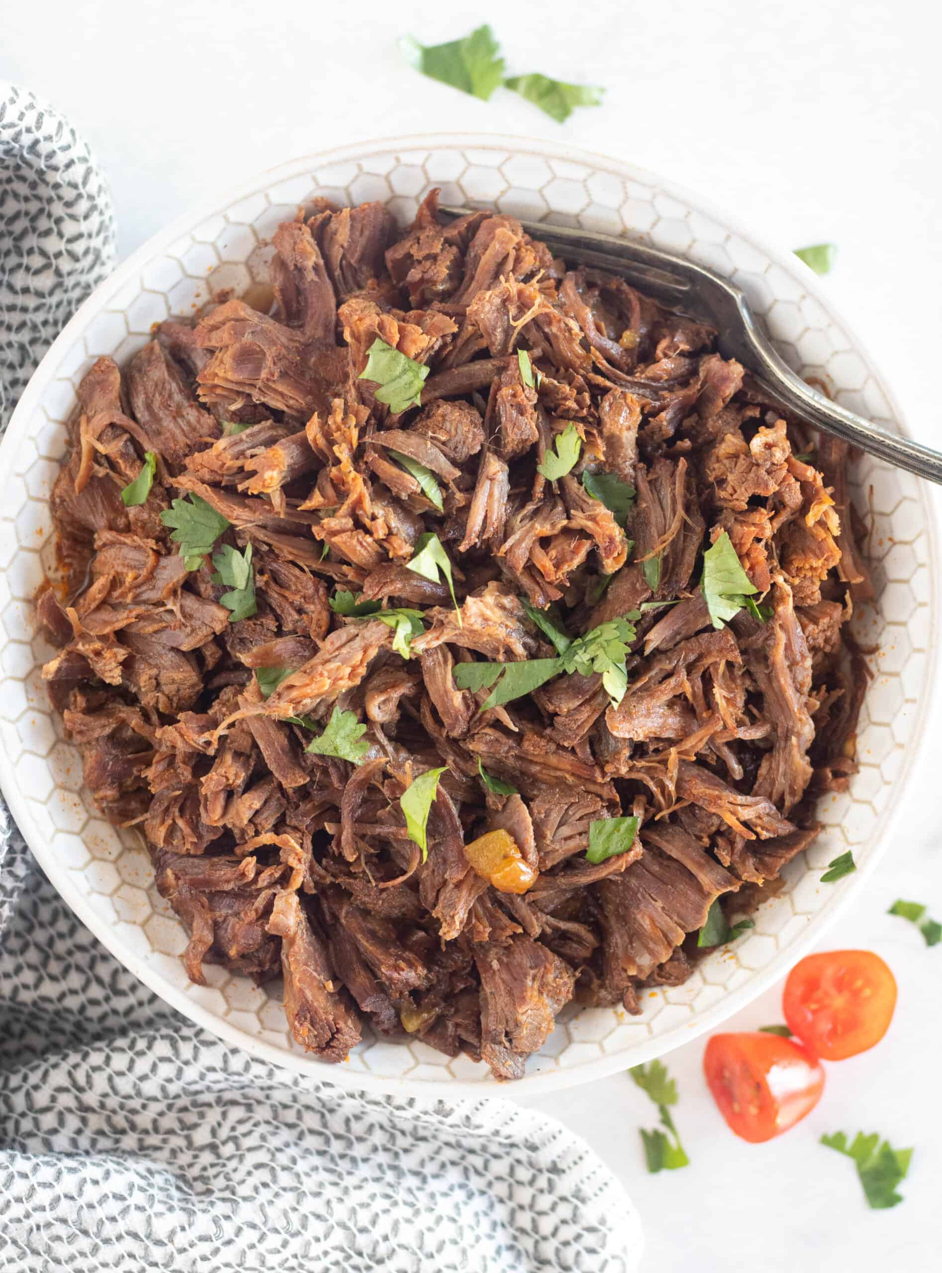shredded beef in a bowl with a fork and garnishes.