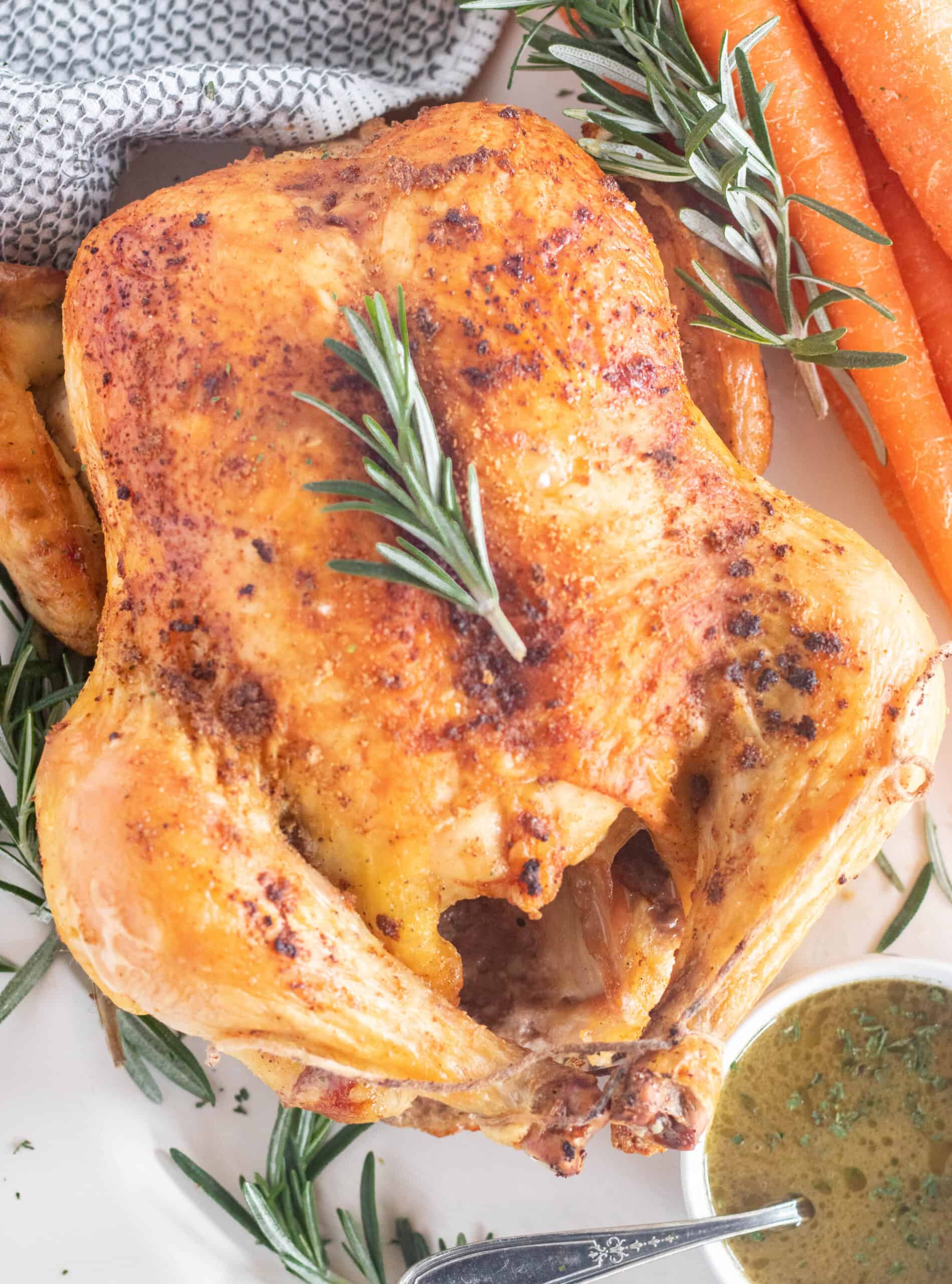 roasted chicken on a platter with rosemary, sauce, and carrots.