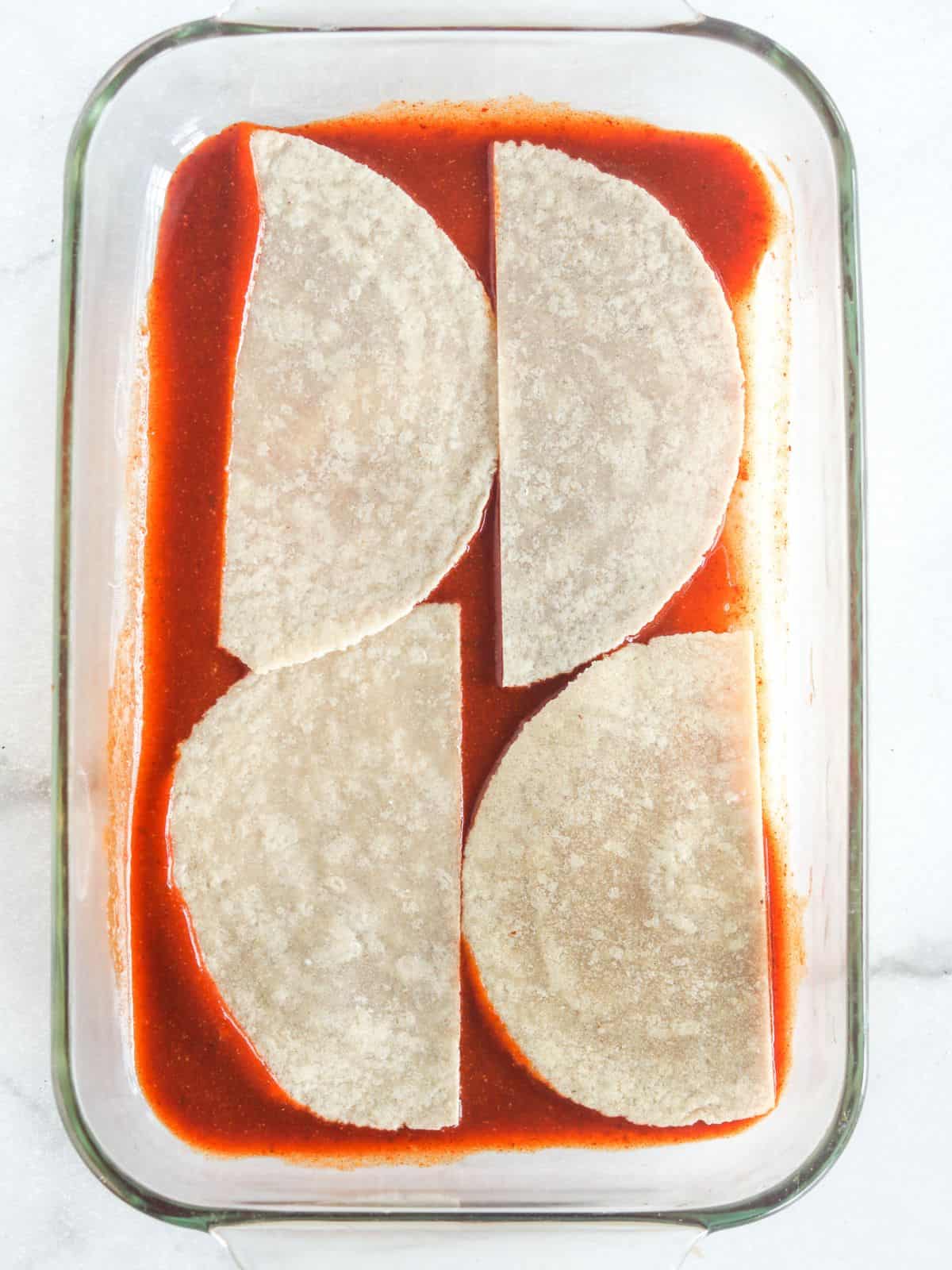 enchilada sauce and tortillas in the bottom of a casserole dish.