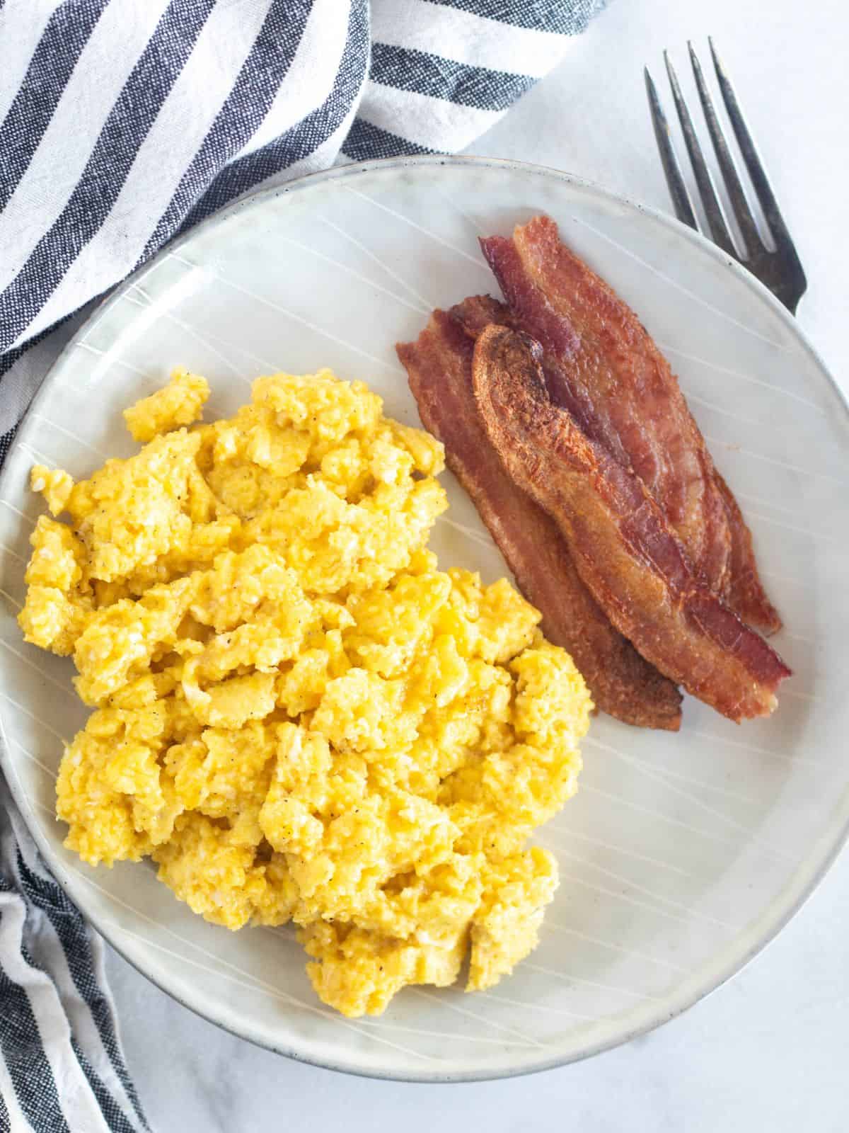 cheesy scrambled eggs on a plate with bacon.