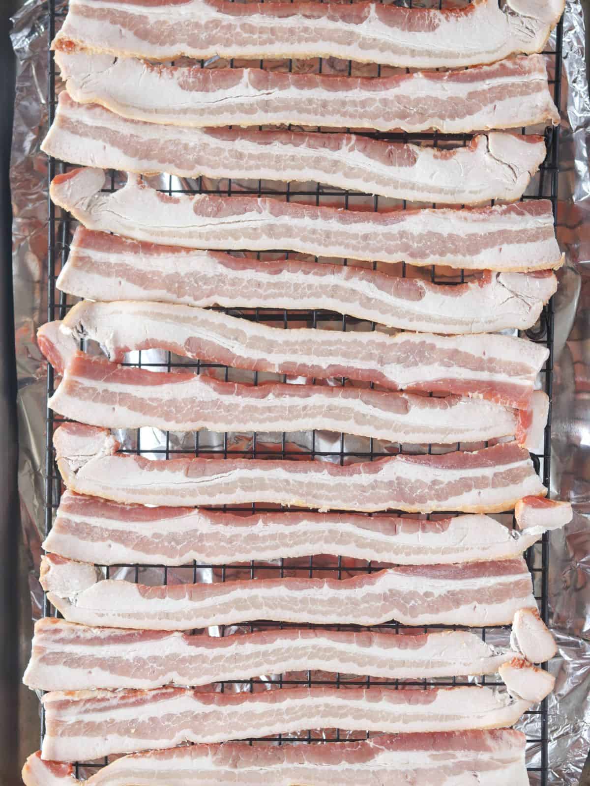 uncooked bacon on a cooling rack in a baking sheet.